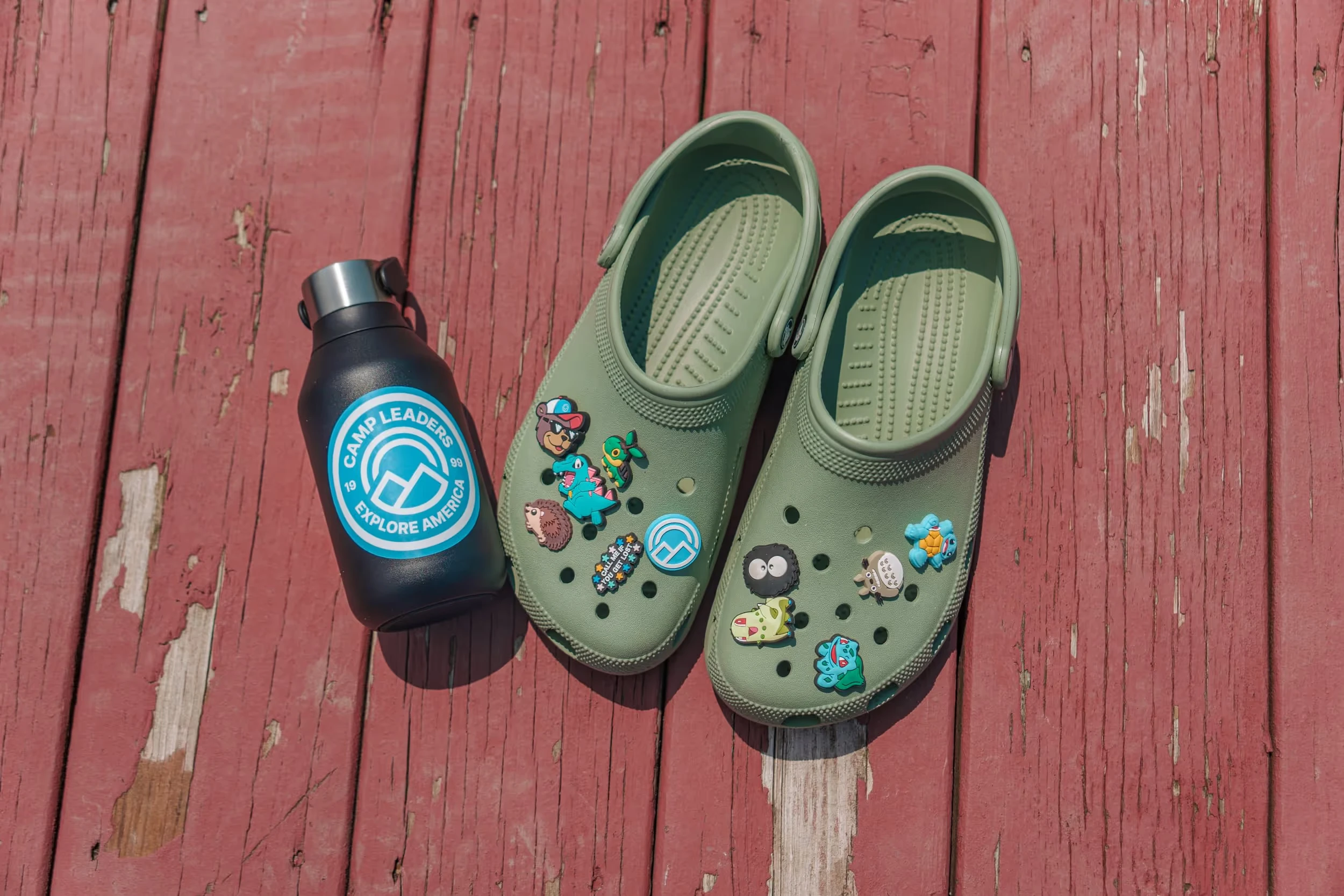 Camp Leaders branded water bottle and Crocs on a red wooden deck